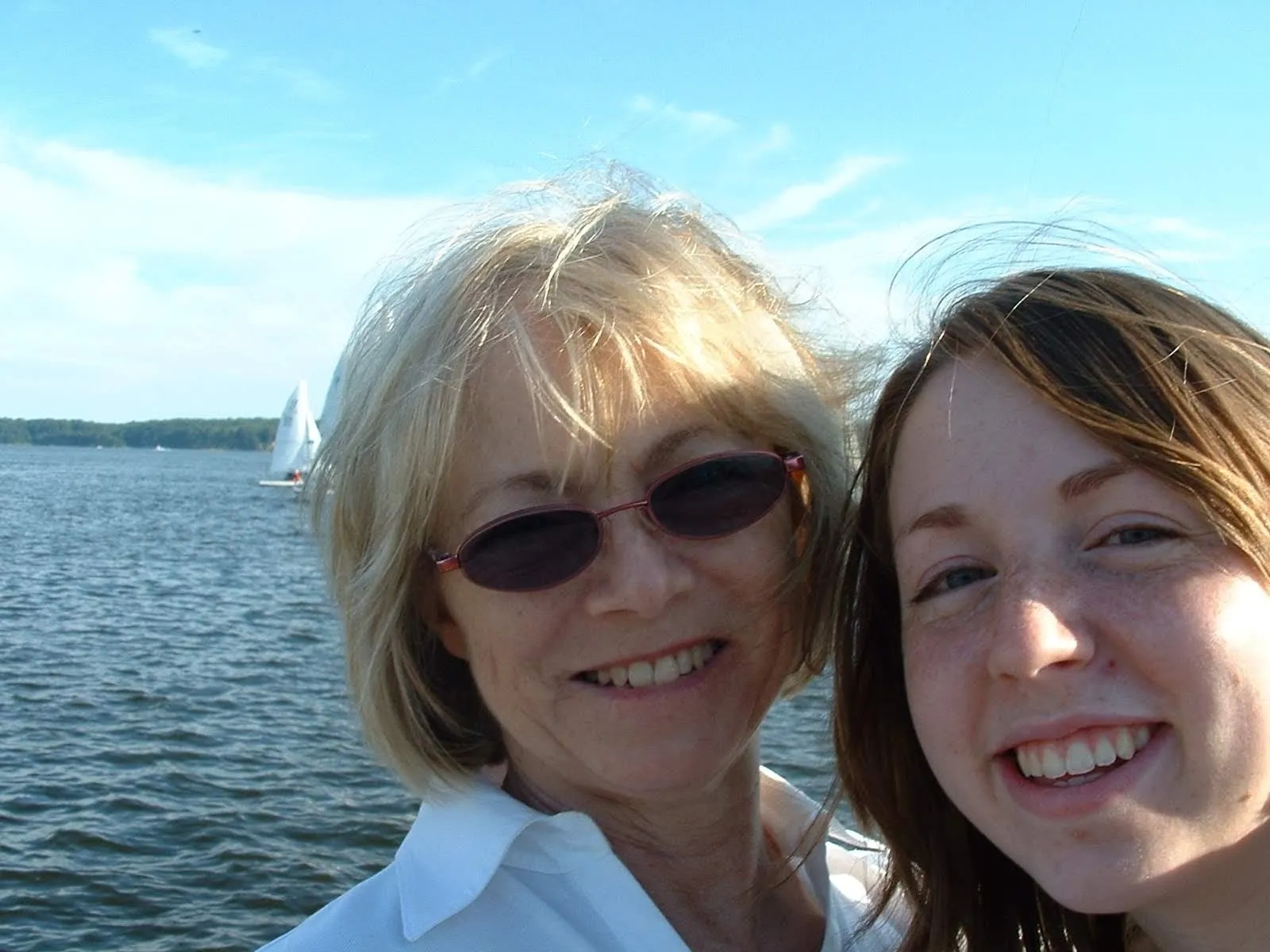Suzanne in sunglasses beside her daughter Dara, water and sailboats behind them